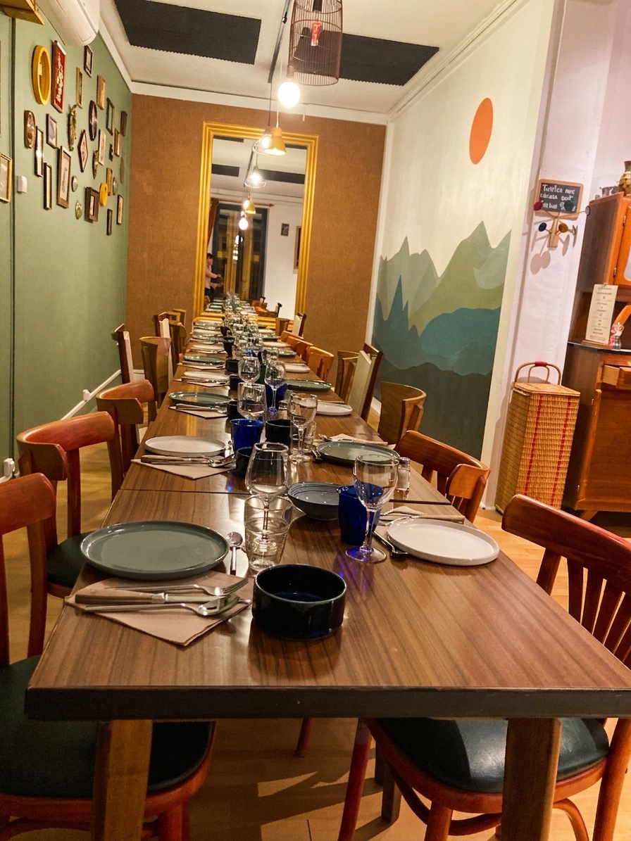 Grande tablée dressée le soir devant la fresque de montagnes, cantine Chez les Filles à Saintes